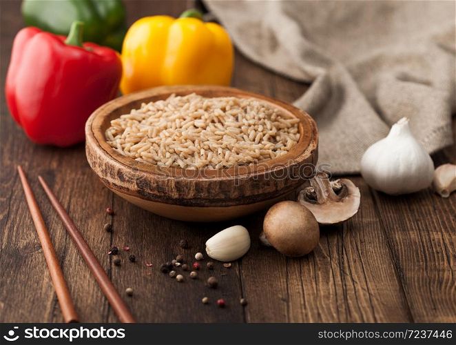 Wooden bowl with boiled long grain risotto rice with mushrooms on wooden background with sticks and linen kitchen towel and paprika pepper with garlic.