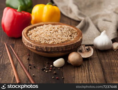 Wooden bowl with boiled long grain risotto rice with mushrooms on wooden background with sticks and linen kitchen towel and paprika pepper with garlic.