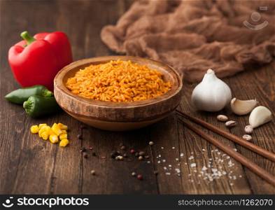 Wooden bowl with boiled red long grain basmati rice with vegetables on wooden background with sticks and red paprika with corn,garlic and basil.