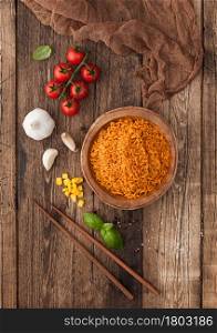 Wooden bowl with boiled red long grain basmati rice with vegetables on wooden table background with sticks and tomatoes with corn,garlic and basil.