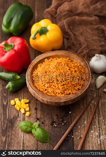 Wooden bowl with boiled red long grain basmati rice with vegetables on wooden background with sticks and paprika pepper with corn,garlic and basil.