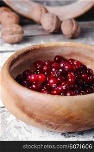 Wooden bowl with cranberries on a wooden background with kitchen smeared with flour. Ripe cranberries in bowls