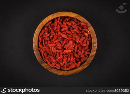 wooden bowl with goji berries on dark stone background