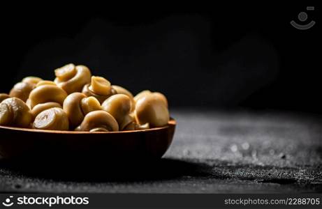 Wooden bowl with pickled mushrooms. On a black background. High quality photo. Wooden bowl with pickled mushrooms.