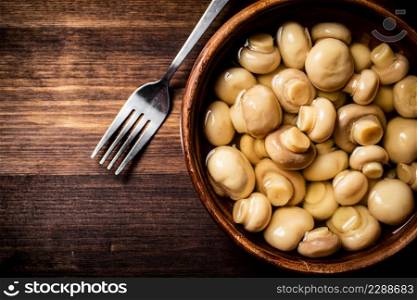 Wooden bowl with small pickled mushrooms. On a wooden background. High quality photo. Wooden bowl with small pickled mushrooms.
