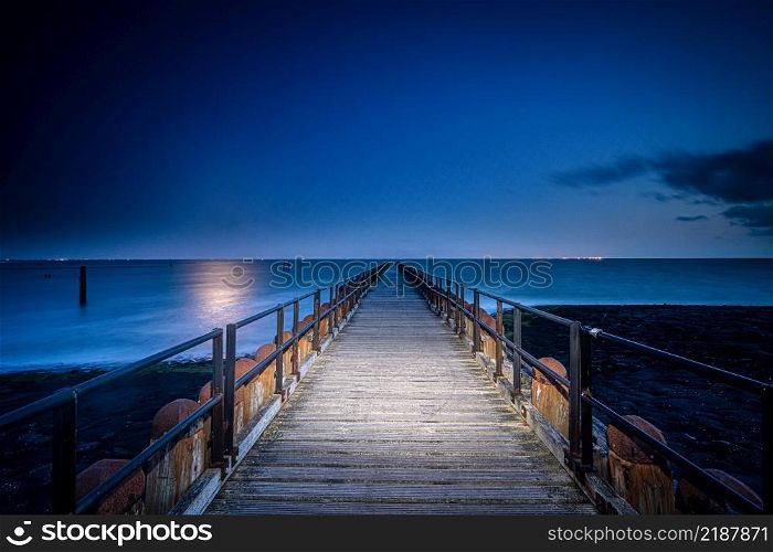 Wooden breakwater with jetty on the sandy beaches of Walcheren near the village of Westkapelle in Zeeland, the Netherlands. Beautiful shot of a long jetty/pier at night. Minimal image with jetty in the center stretching to the ocean.