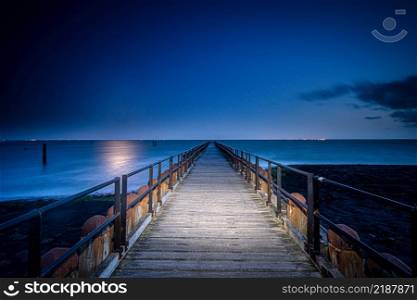 Wooden breakwater with jetty on the sandy beaches of Walcheren near the village of Westkapelle in Zeeland, the Netherlands. Beautiful shot of a long jetty/pier at night. Minimal image with jetty in the center stretching to the ocean.