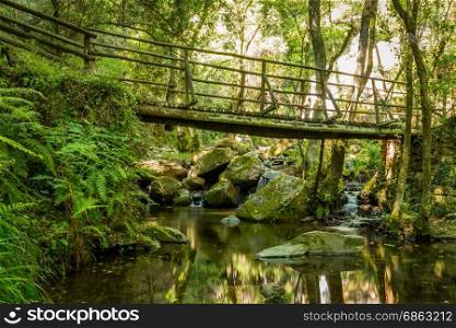 Wooden bridge near beautiful waterfall in Cabreia Portugal. Long exposure smooth effect.