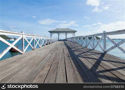 Wooden bridge stretching into the sea. Small boats moored nearby.