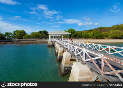 Wooden bridge stretching into the sea. Small boats moored nearby.