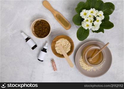 wooden brush honey oats himalayan rock salt essential oil bottle with primula flowers vase concrete background