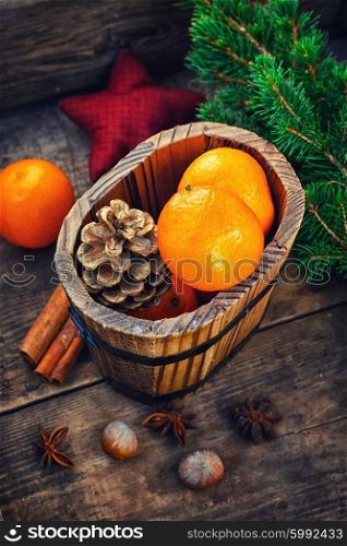 Wooden bucket with tangerines. Wooden bucket with tangerines and pine cones on the background of Christmas trees and spices