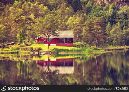 Wooden cabin hytte in norwegian green forest on water lake shore. Beautiful landscape in Norway, Scandinavia. wooden cabin in forest on lake shore, Norway