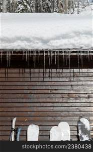 Wooden cabin with snowy roof and icicles and ski equipment equipment leaning against the wallat sunny winter day, close up