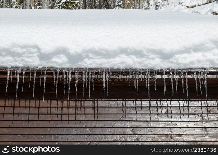 Wooden cabin with snowy roof and icicles at sunny winter day, close up
