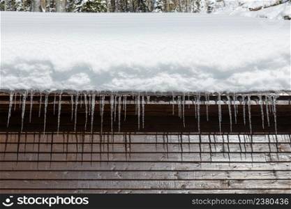 Wooden cabin with snowy roof and icicles at sunny winter day, close up