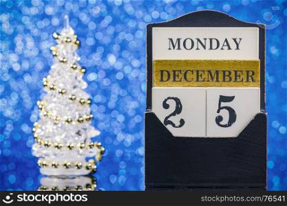 Wooden calendar and Christmas tree reflection on glass table over blue background
