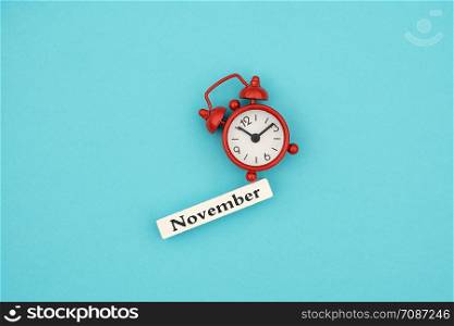 Wooden calendar autumn month November and red alarm clock on blue paper background. Concept Hello September. Creative Top view Flat Lay Minimal style.. Wooden calendar autumn month November and red alarm clock on blue paper background. Concept Hello September. Creative Top view Flat Lay Minimal style