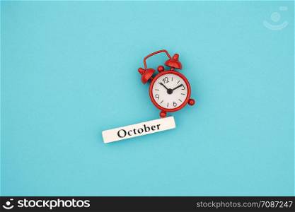 Wooden calendar autumn month October and red alarm clock on blue paper background. Concept Hello September. Creative Top view Flat Lay Minimal style.. Wooden calendar autumn month October and red alarm clock on blue paper background. Concept Hello September. Creative Top view Flat Lay Minimal style