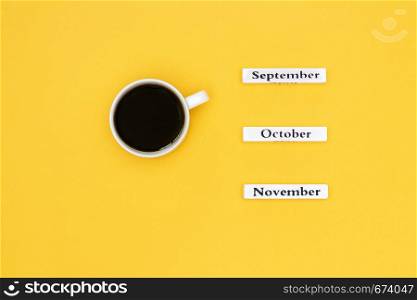 Wooden calendar autumn months September October November and Cup of black coffee aimed at September on yellow background. Concept Top view Flat Lay Copy space. Cup of coffee and calendar November October September on yellow background