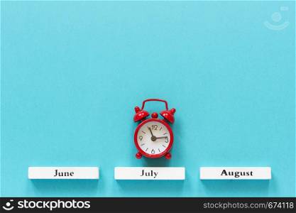 Wooden calendar summer months and red alarm clock over July on blue background. Concept July time Creative Top view Flat Lay Minimal style Copy space.. Wooden calendar summer months and red alarm clock over July on blue background. Concept July time Creative Top view Flat Lay Minimal style Copy space