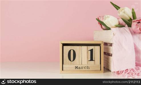 wooden calendar with 1st march near crate with tulips scarf desk against pink background