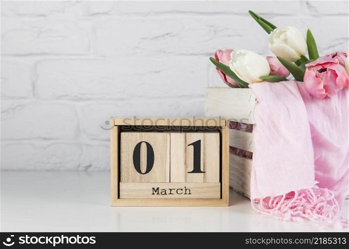 wooden calendar with 1st march near wooden crate with tulips scarf white desk