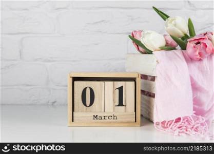 wooden calendar with 1st march near wooden crate with tulips scarf white desk