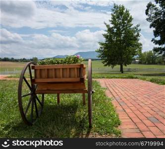 Wooden cart containing flowers and blossoms by brick path in landscape