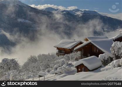 wooden chalets in alpine village covered with snow in mountain landscape
