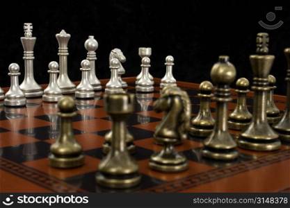 Wooden chess board with metal peices. Shot in studio on black from corner to corner. Focus on light pieces.
