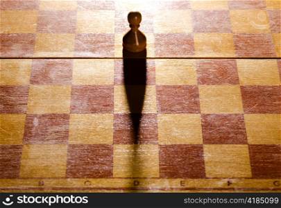 wooden chess pawn is standing on board with long shadow
