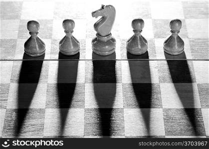 wooden chess pieces are standing on board with long shadows