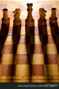 wooden chess pieces are standing on board with long shadows