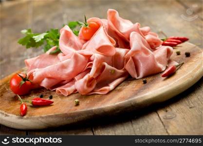 wooden chopping board with sliced mortadella and red pepper
