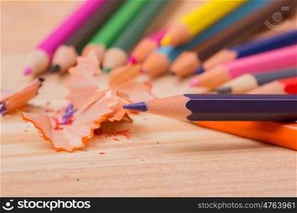 Wooden colorful pencils with sharpening shavings, on wooden table