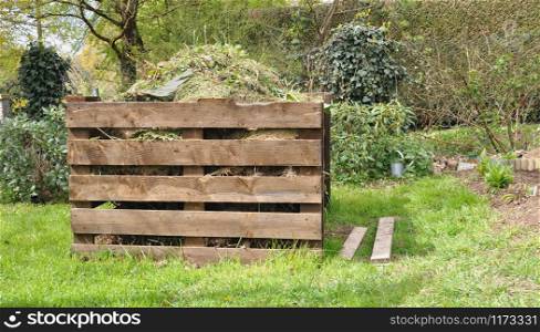 wooden composter full of waste in a garden