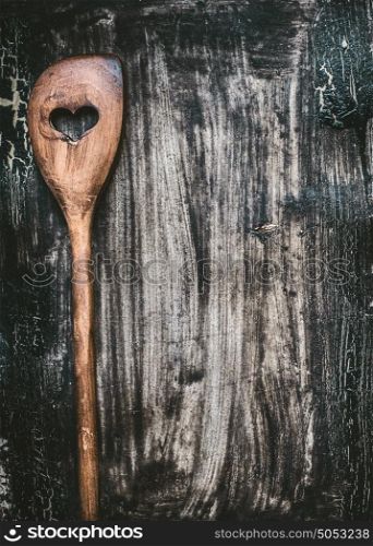 Wooden cooking spoon with heart on dark rustic background, top view. Food background for recipes, menu or list