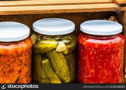 Wooden crate with glass jars with variety of canned vegetables isolated.
