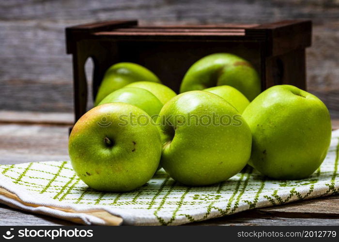 Wooden crate with ripe green apples on wooden table.