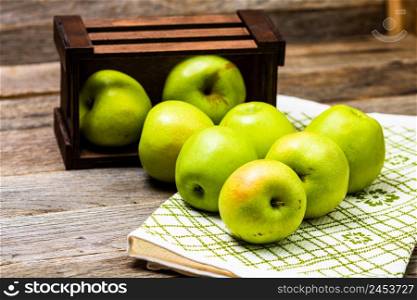 Wooden crate with ripe green apples on wooden table.