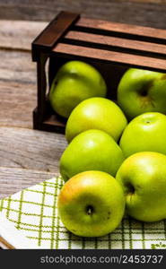 Wooden crate with ripe green apples on wooden table.