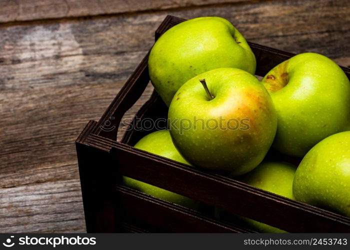 Wooden crate with ripe green apples on wooden table.