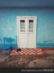 Wooden crutch and a pair of old footwear on threshold, doorstep of a rustic house. Traditional rural building facade in Moldova. Blue lime painted walls and white colored door. Vintage home details.