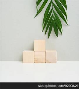 Wooden cube on a gray background with a green palm leaf. Stage for product demonstration, cosmetics. Promotion and advertising