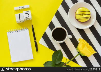 Wooden cubes calendar April 15th. Cup of coffee, yellow donut and rose on black and white napkin, empty open notepad for text on yellow background. Concept stylish workplace Top view Flat lay Mockup. Wooden cubes calendar April 15th. Cup of coffee, yellow donut and rose on black and white napkin, empty open notepad for text on yellow background. Concept stylish workplace