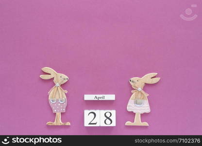 Wooden cubes calendar April 28 and pair of wooden easter bunnies on purple paper background. Concept Christian Easter Copy space Template for lettering, text or your design Creative Top View.. Wooden cubes calendar April 28 and pair of wooden easter bunnies on purple paper background. Concept Christian Easter Copy space Template for lettering, text or your design Creative Top View