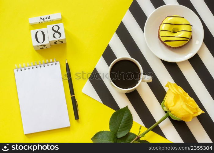 Wooden cubes calendar April 8th. Cup of coffee, yellow donut and rose on black and white napkin, empty open notepad for text on yellow background. Concept stylish workplace Top view Flat lay Mockup. Wooden cubes calendar April 8th. Cup of coffee, yellow donut and rose on black and white napkin, empty open notepad for text on yellow background. Concept stylish workplace