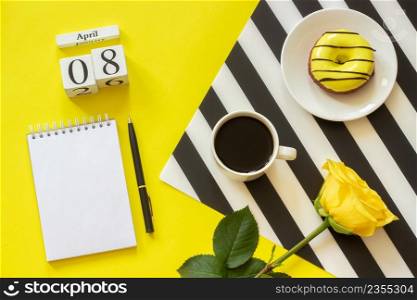 Wooden cubes calendar April 8th. Cup of coffee, yellow donut and rose on black and white napkin, empty open notepad for text on yellow background. Concept stylish workplace Top view Flat lay Mockup. Wooden cubes calendar April 8th. Cup of coffee, yellow donut and rose on black and white napkin, empty open notepad for text on yellow background. Concept stylish workplace