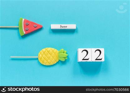 Wooden cubes calendar date June 22nd and summer fruits candy pineapple, watermelon lollipops on stick on blue background. Concept vacation or holidays Creative Top view Flat lay Template.. Wooden cubes calendar date June 22nd and summer fruits candy pineapple, watermelon lollipops on stick on blue background. Concept vacation or holidays Creative Top view Flat lay Template